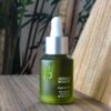 Close-up of Herban Wisdom facial oil bottle on a wooden table, natural setting.