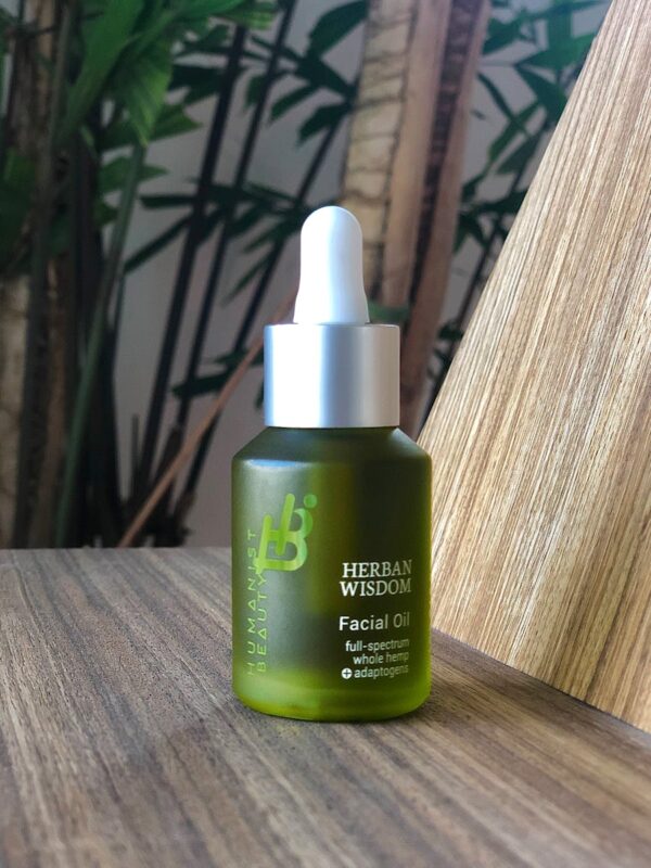 Close-up of Herban Wisdom facial oil bottle on a wooden table, natural setting.