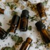 Brown glass bottles of essential oils surrounded by dried herbs on a white surface.