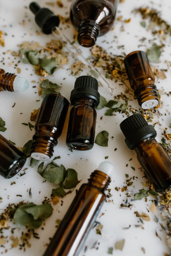 Brown glass bottles of essential oils surrounded by dried herbs on a white surface.