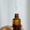A hand holding a brown glass bottle with a dropper against a white background.