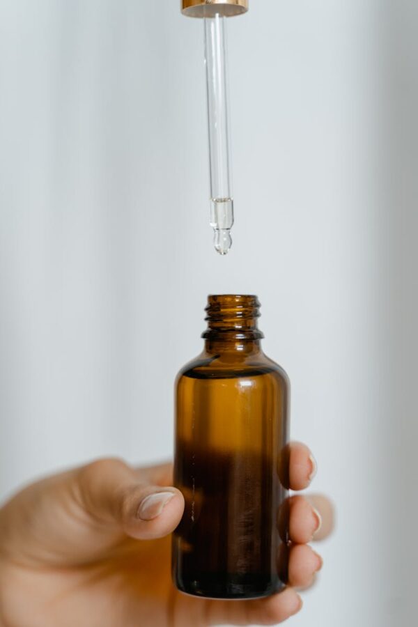 A hand holding a brown glass bottle with a dropper against a white background.