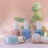 Elegant pastel nail polish bottles with green leaves in a soft, natural setting.