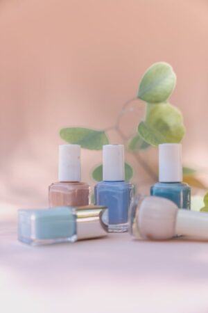 Elegant pastel nail polish bottles with green leaves in a soft, natural setting.